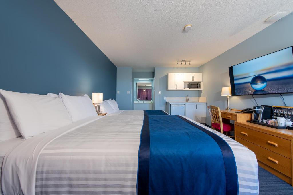 a bedroom with a large bed and a desk and a kitchen at Ocean Crest Motel in Qualicum Beach