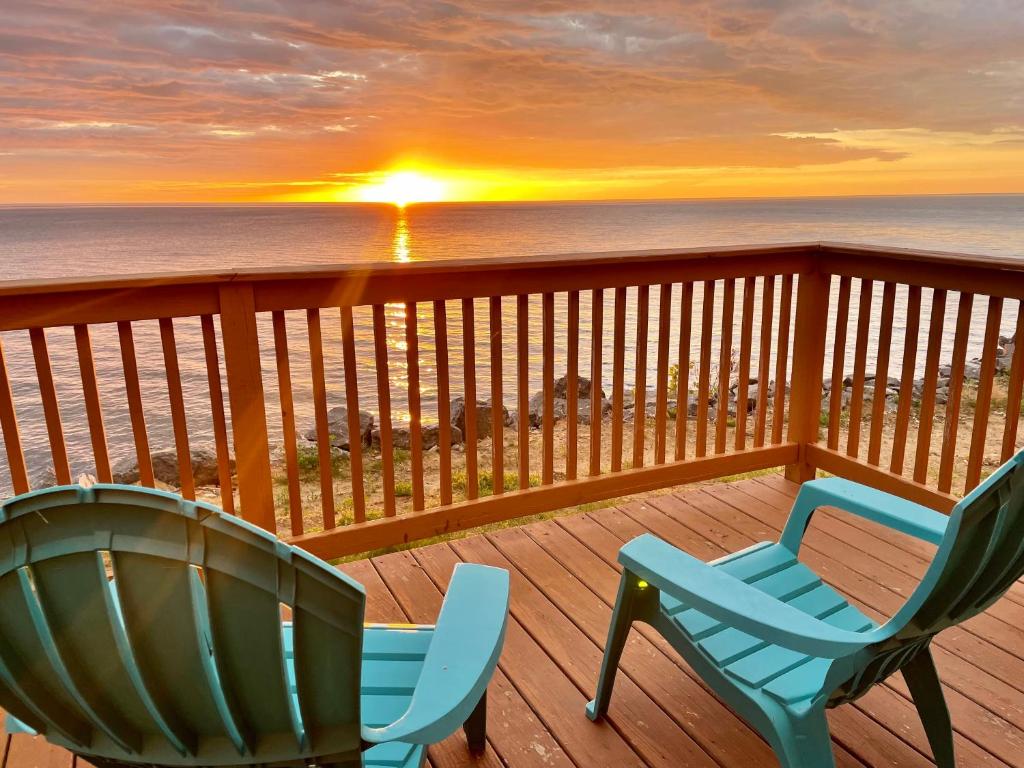 two chairs on a deck with a sunset over the ocean at Cozy LAKE ONTARIO WATERFRONT Breathtaking Views! in Pulaski