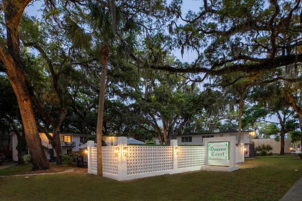 a white fence with a sign in a yard with trees at Queen's Court Inn in Saint Simons Island