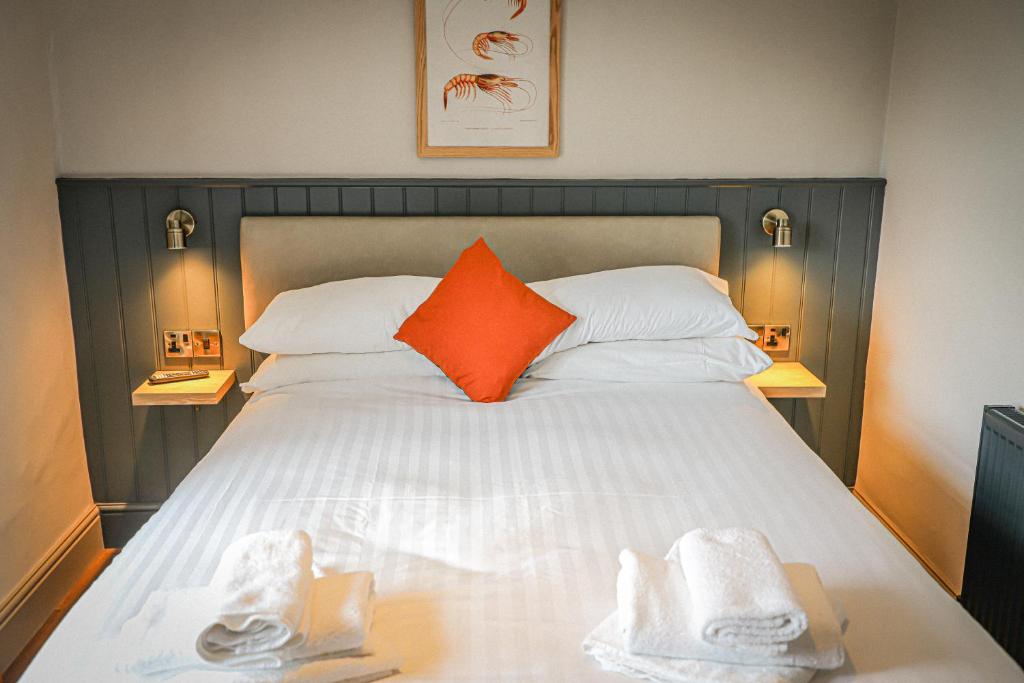 Una cama con una almohada naranja y toallas. en Hope and Anchor, en Flookburgh