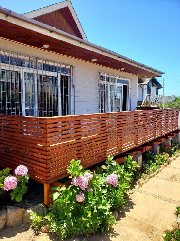 a house with a wooden deck with flowers in front of it at Acogedora casa en la playa in El Quisco