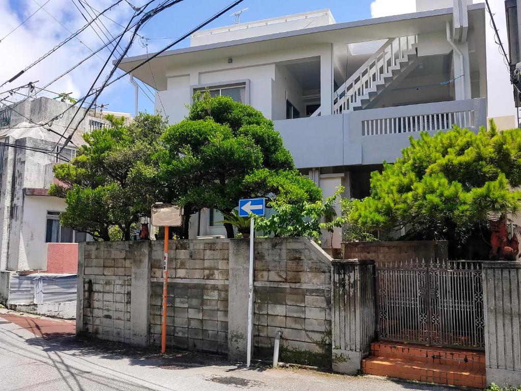 a house with a fence and a blue sign in front of it at 最大14人 駐車縦列4台可能 個室4部屋 広々戸建て 国際通りと牧志駅まで徒歩5分 わらゆんＳｏヴィラ壺屋 in Naha