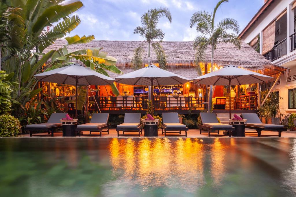 a resort with a pool and chairs and umbrellas at La Bastide de Caro in Siem Reap