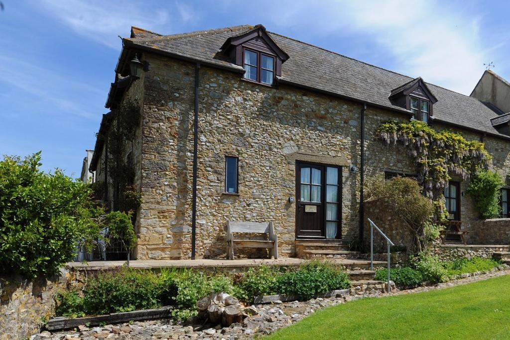 een oud stenen huis met een bankje ervoor bij Rose Cottage in Musbury