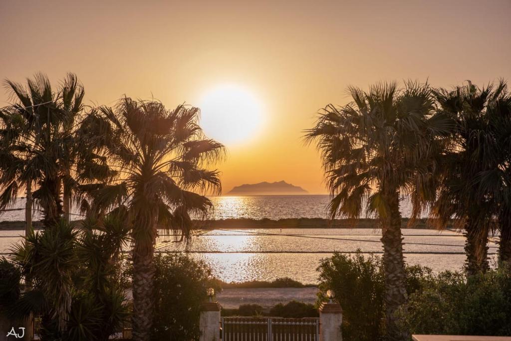 un coucher de soleil sur l'eau avec des palmiers dans l'établissement Casita Spagnola, à Marsala