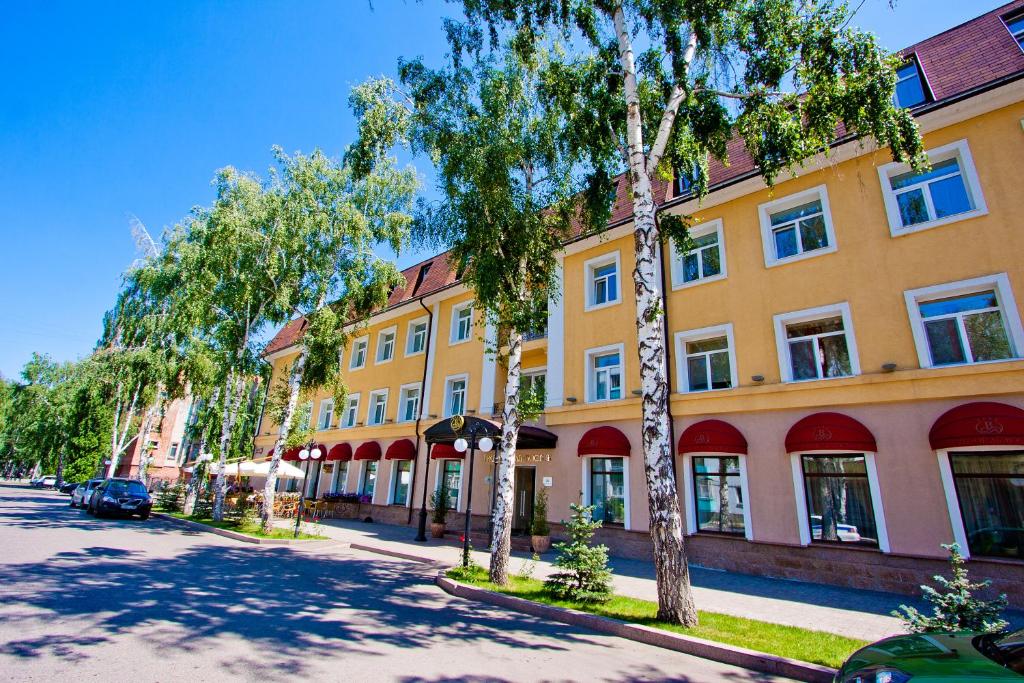 a yellow building with trees in front of a street at Grand Hotel Vostok in Sterlitamak