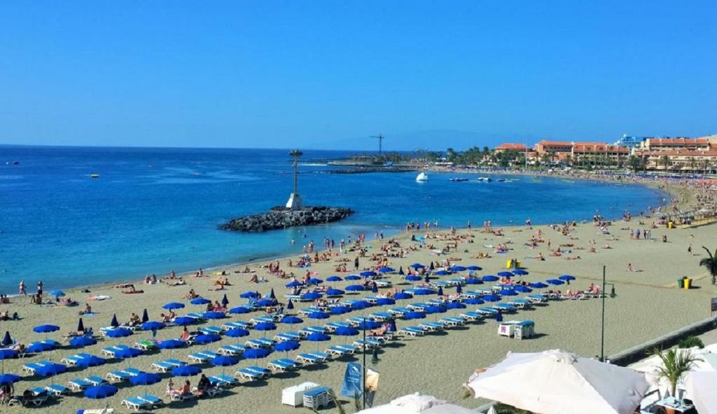 a beach with a lot of people and blue umbrellas at Canarian Garden Building Jardines Canarios in Los Cristianos