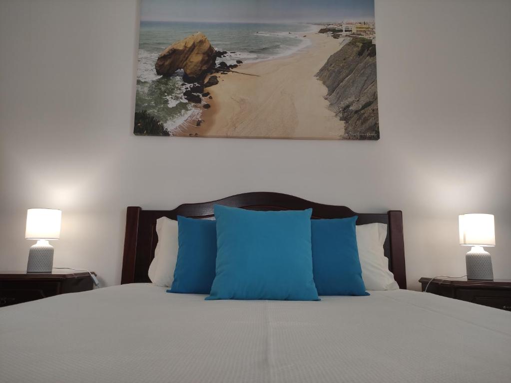 a bed with blue pillows and a picture of a beach at Casa S Nicolau 1 Near the beach in Lourinhã