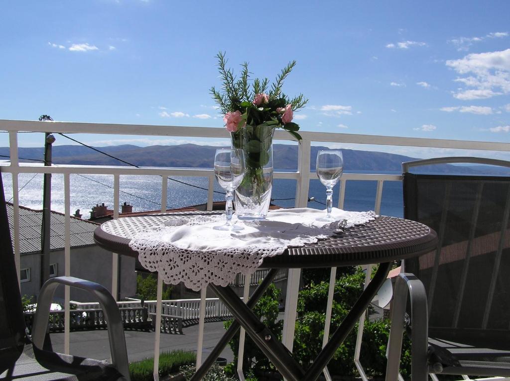 uma mesa com copos e um vaso de flores numa varanda em Guest House Adria em Senj