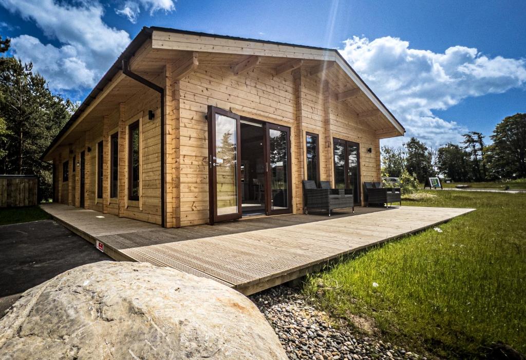 uma pequena casa num deque de madeira com uma grande rocha em Sundance Lodge, Fantastic New Cabin with Hot Tub - Sleeps 6 - Largest In Felmoor Park em Morpeth