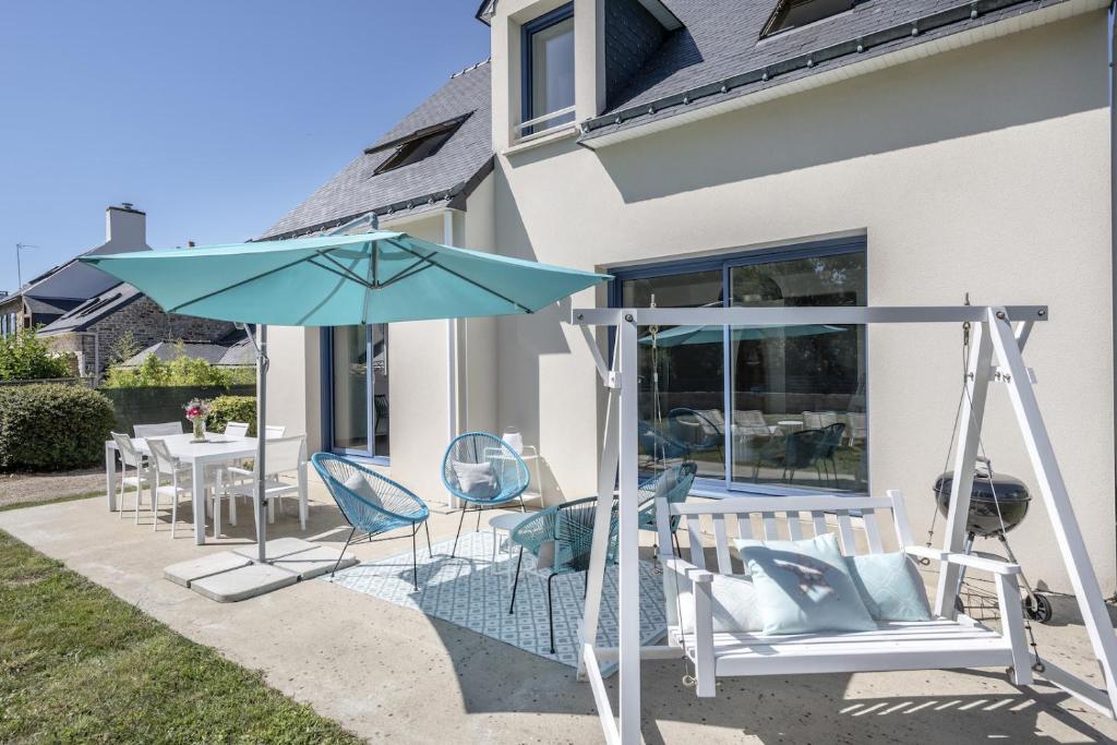 a patio with a swing and an umbrella and chairs at Maison vue mer dans le Golfe du Morbihan in Baden