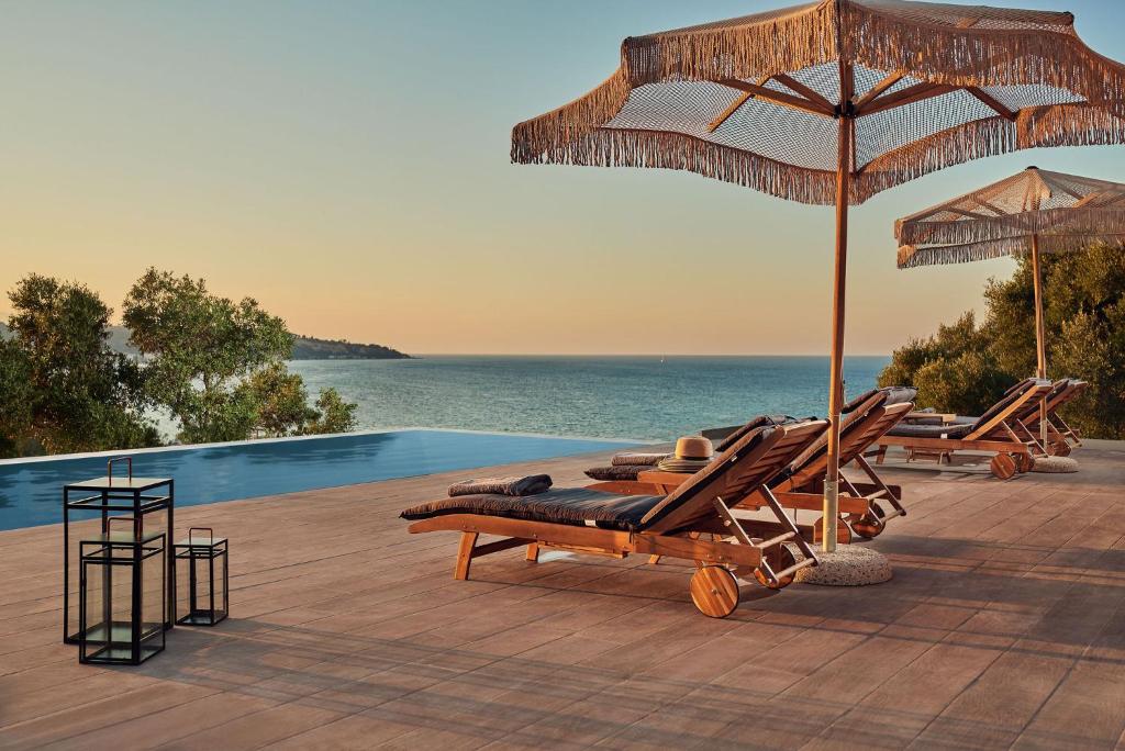 a group of lounge chairs and an umbrella next to a pool at Althea Lavish Estate - Villa & Suite in Zakynthos Town