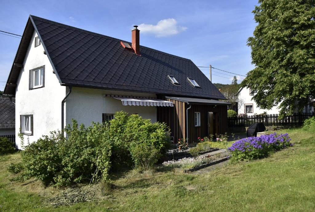 une maison blanche avec un toit noir et quelques fleurs dans l'établissement Chalupa Abecha, à Dolní Poustevna