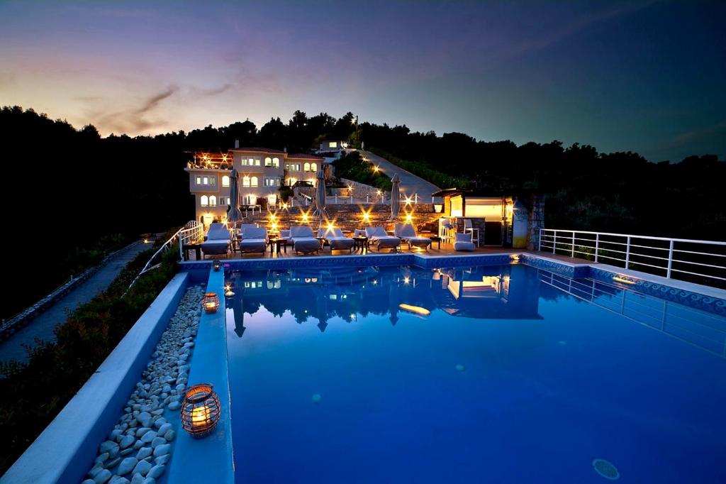una piscina di fronte a una casa di notte di GoldenHill Studios&apartments a Città di Skiathos