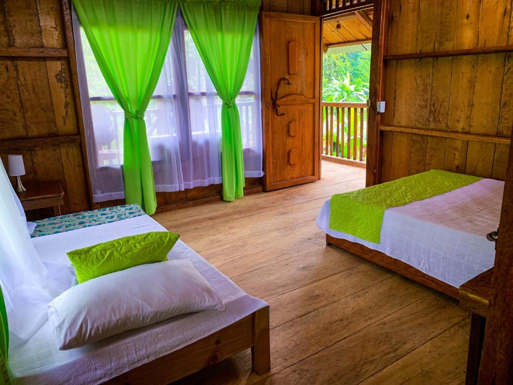 2 camas en una habitación con cortinas verdes en Mama Yeya raíces, en San Cipriano