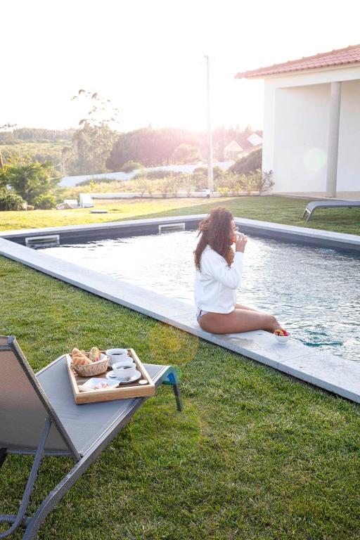 a woman sitting on the edge of a swimming pool at Refúgio da Rainha in Moledo