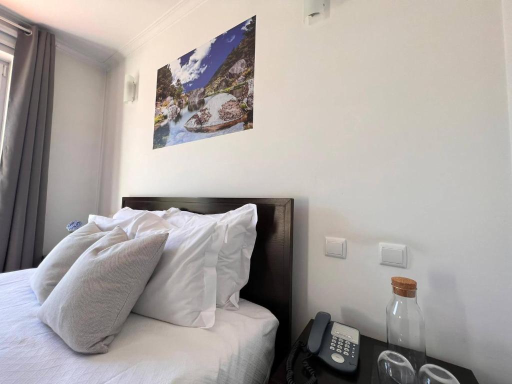 um quarto com uma cama com almofadas brancas e um telefone em Vale do Zêzere Hotel em Manteigas