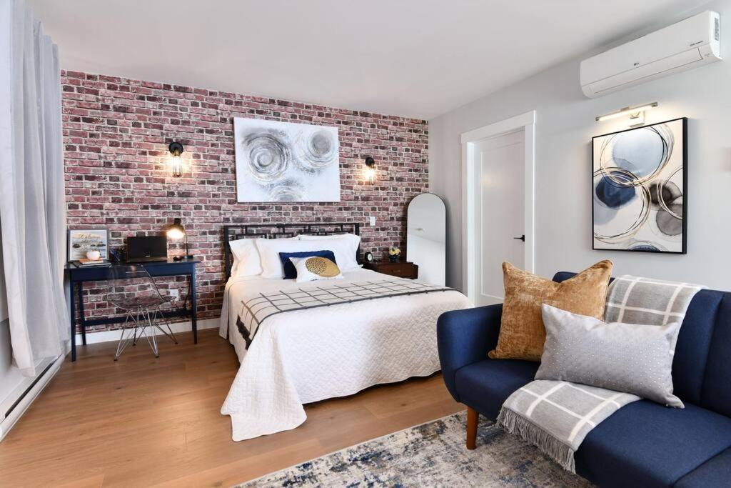 Jardin Suites Highfield في مونكتون: غرفة نوم بحائط من الطوب وسرير واريكة