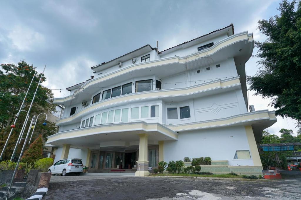 un edificio blanco con un coche aparcado delante de él en Urbanview Hotel Pangkalpinang by RedDoorz en Kebinti