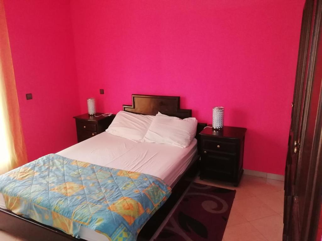 een slaapkamer met roze muren en een bed met 2 nachtkastjes bij Appartement dans villa in Cite Adrar