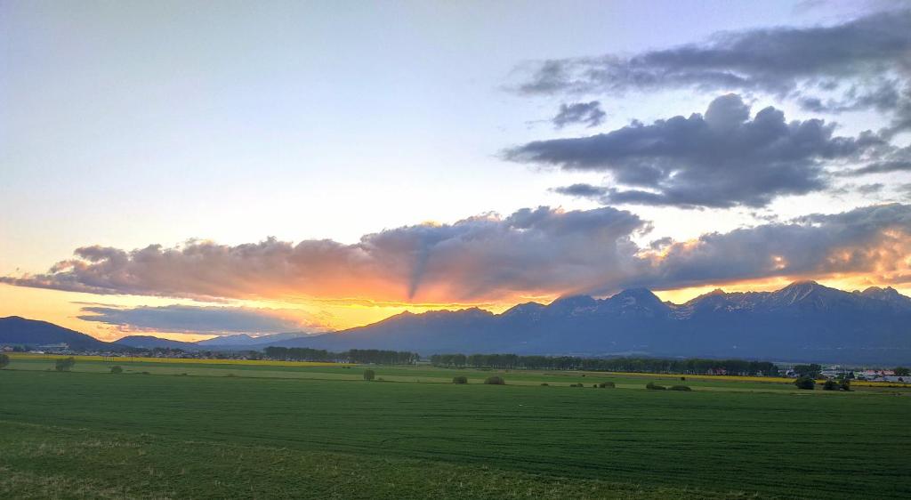 a sunset over a green field with mountains in the background at Sunset Studio Apartment in Poprad