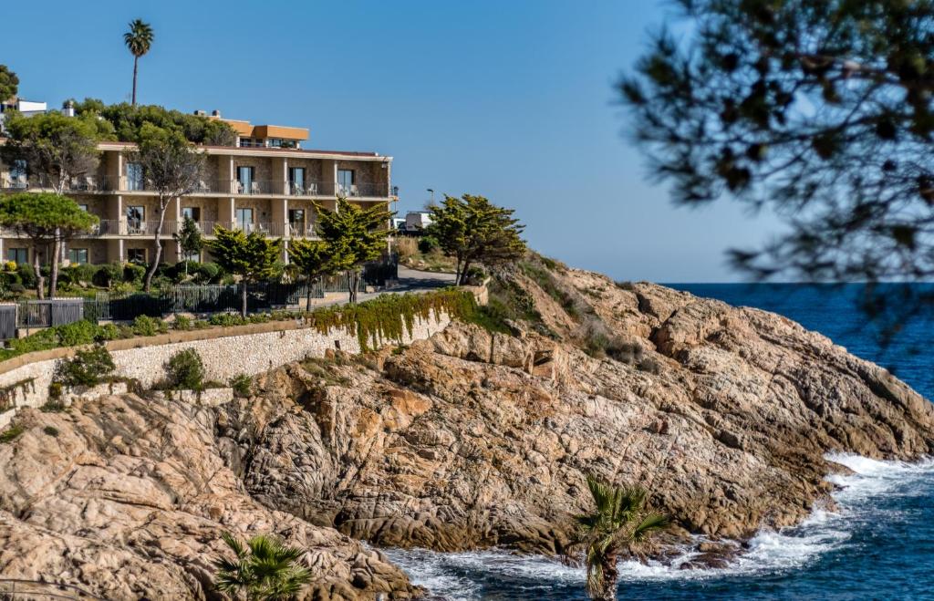 ein Gebäude auf einer Klippe neben dem Wasser in der Unterkunft Eden Roc Hotel & Spa by Brava Hoteles in Sant Feliu de Guixols