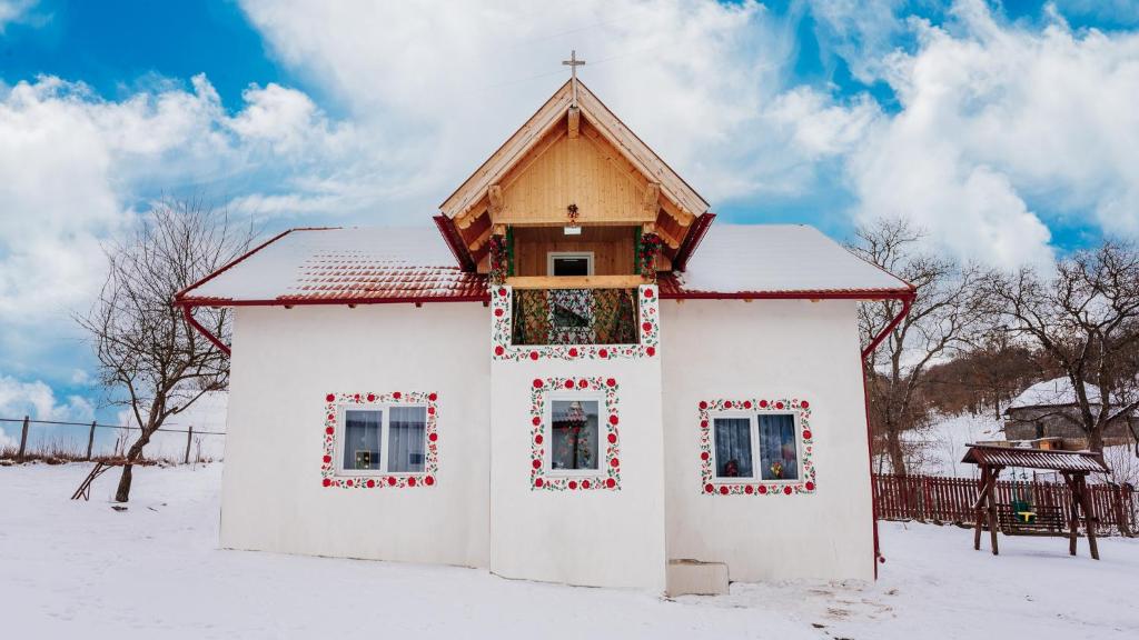 Una pequeña capilla blanca en la nieve con una cruz en CASUTA CU FLORI, en Vîlcele