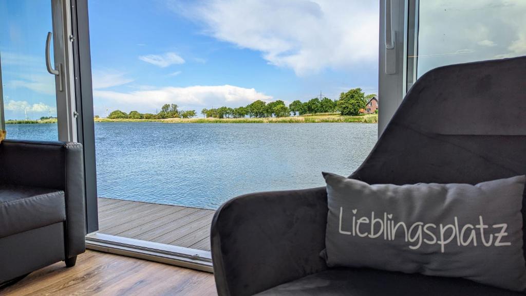 a living room with a chair and a view of a lake at Hausboot Wangermeerblick (Floating Home) in Wangerland