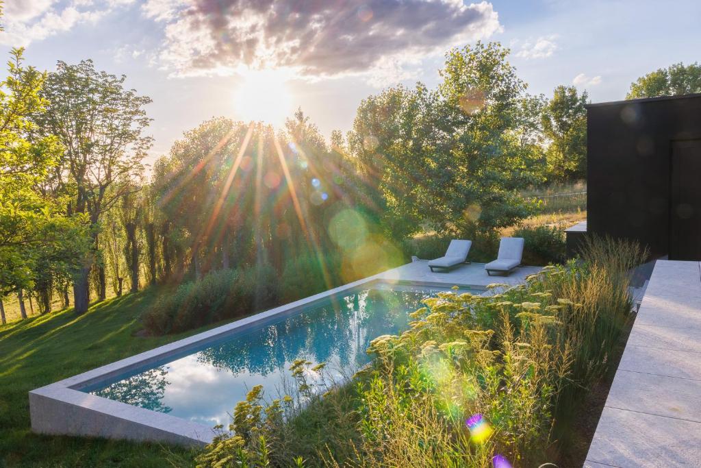 a pool in the middle of a garden with the sun shining at Holiday Home L'O Reine - with luxury wellness in Sint-Pieters-Leeuw
