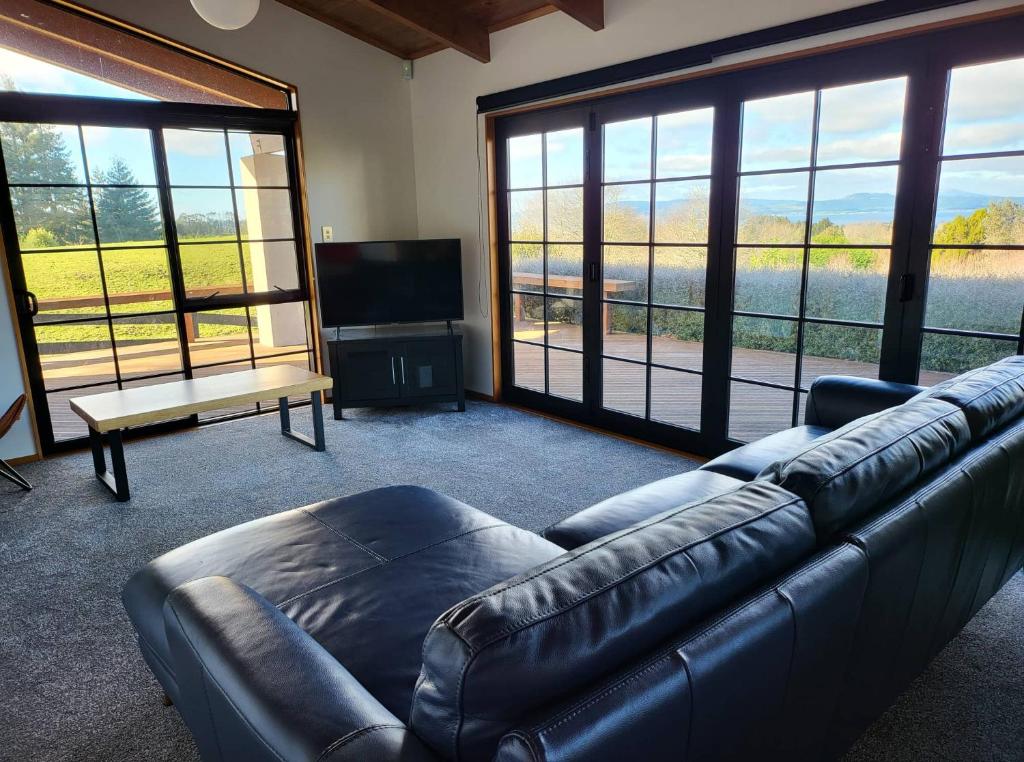 a living room with a leather couch and large windows at Hamurana Home with a View in Rotorua