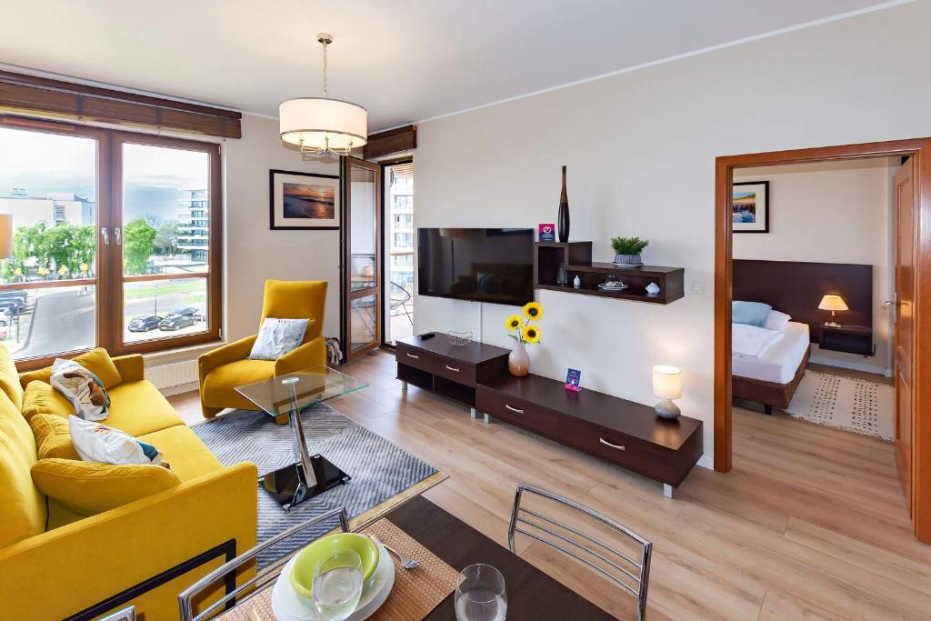 a living room with a yellow couch and a bedroom at VacationClub – Olympic Park Apartament B302 in Kołobrzeg