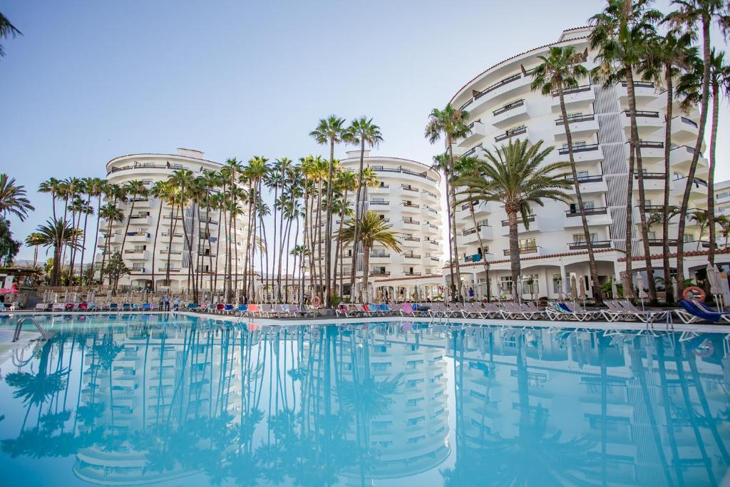 a large swimming pool with palm trees in front of a building at Servatur Waikiki in Playa del Ingles