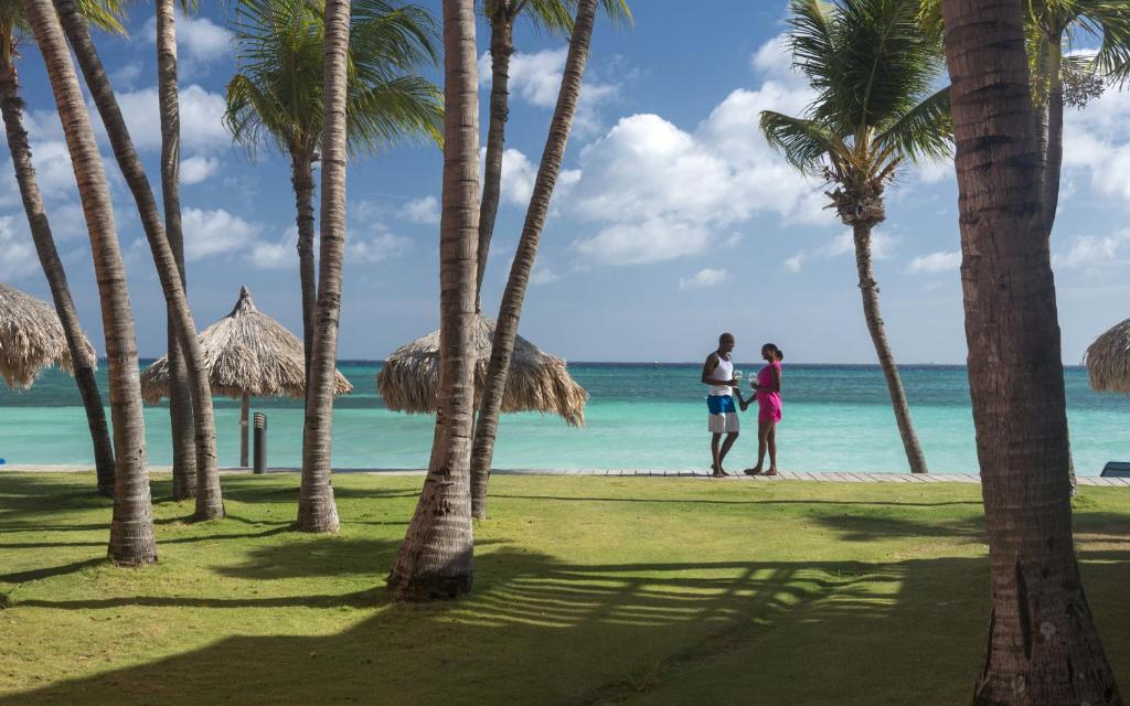 two people standing on a beach next to palm trees at All Inclusive - Divi Dutch Village Beach Resort in Palm-Eagle Beach