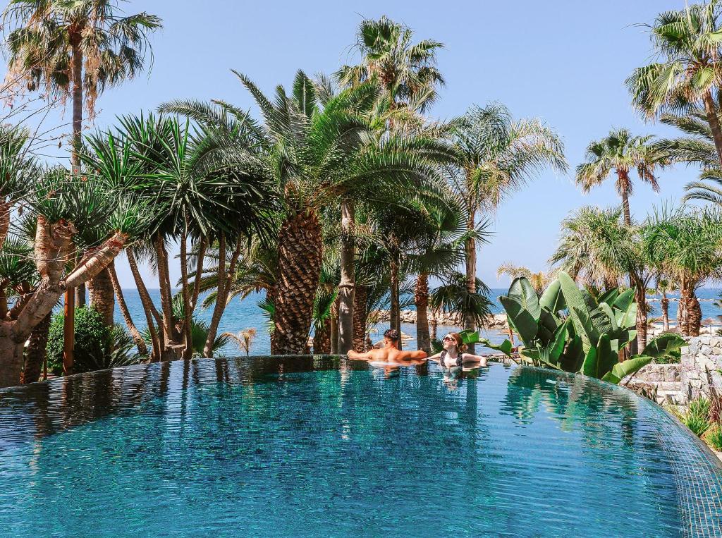 two people laying in a swimming pool with palm trees at Amathus Beach Hotel Limassol in Limassol