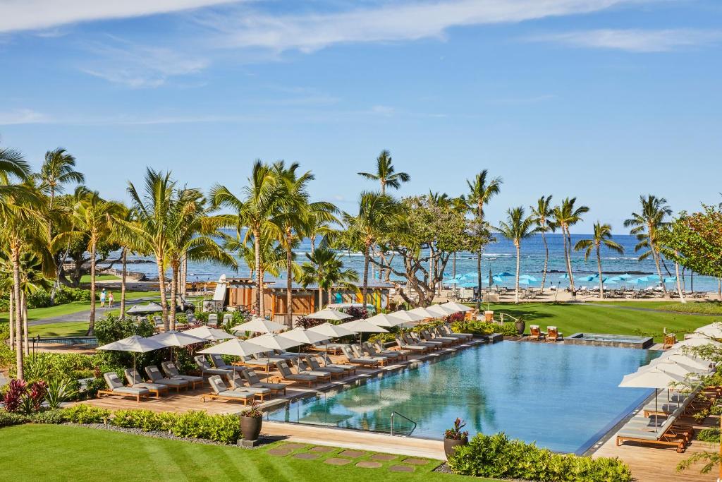 an outdoor pool with umbrellas and chairs and the ocean at Mauna Lani, Auberge Resorts Collection in Waikoloa