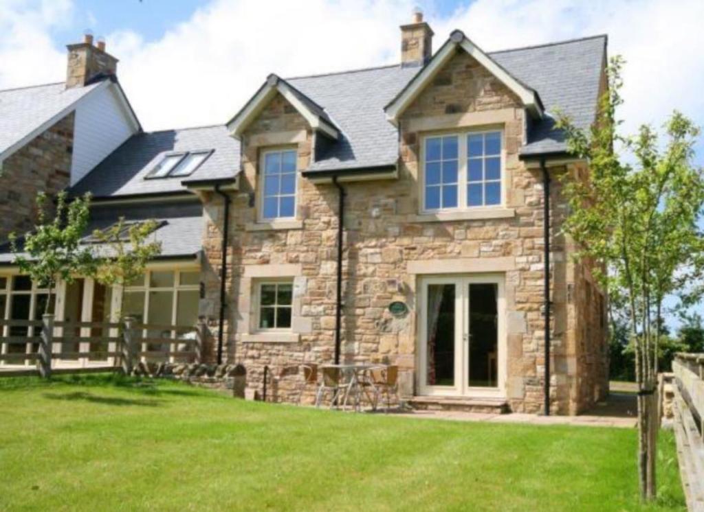 a stone house with a fence in the yard at Northern Hideaways Ellingham in Chathill