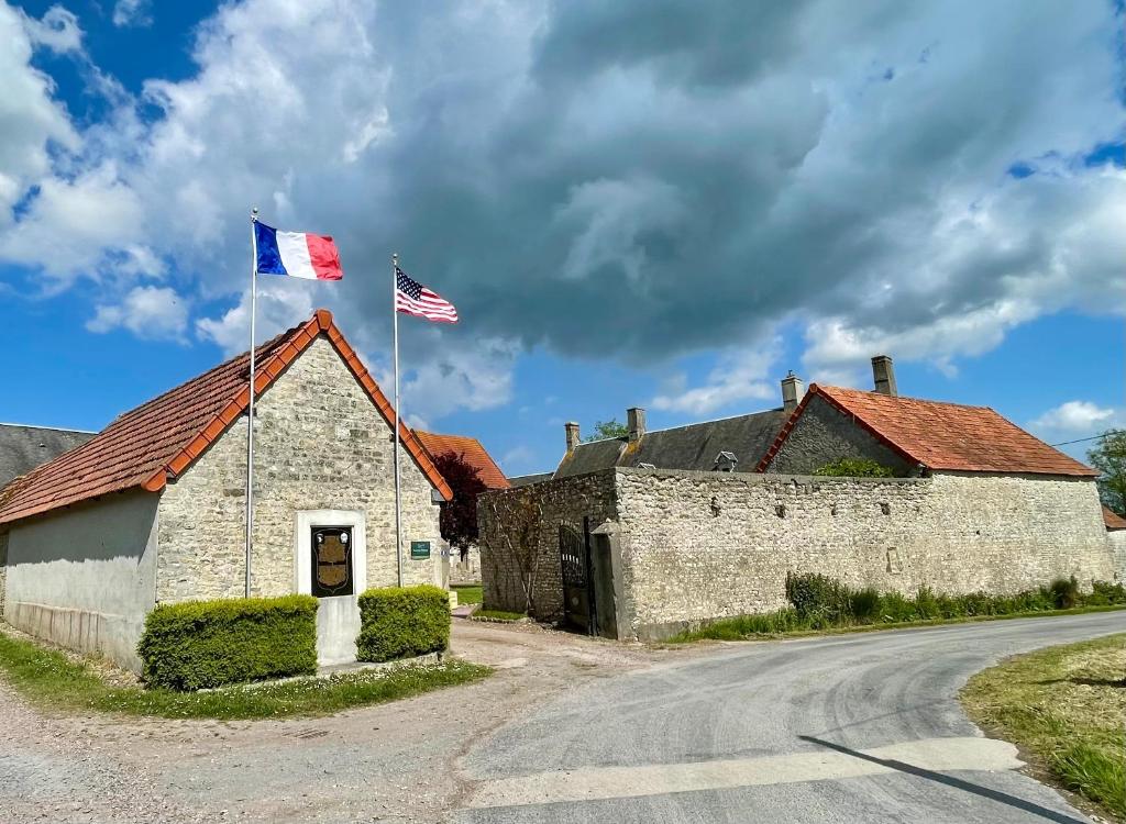 an old stone building with two flags on top of it at La Ferme Delaunay in Saint-Côme-du-Mont