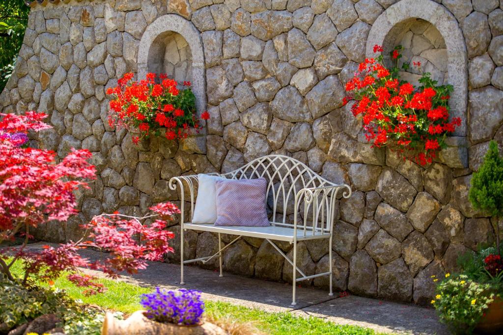 a bench in front of a stone wall with flowers at B&B Marijana in Malinska