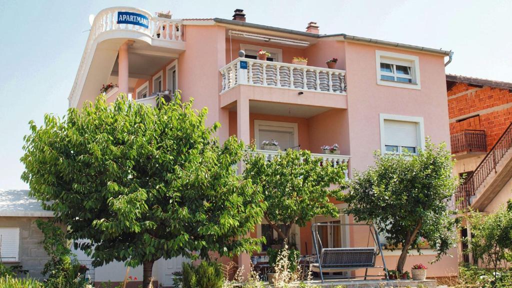 un edificio rosa con árboles delante de él en Apartments Malenica, en Vodice