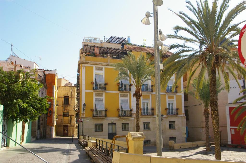 una calle con palmeras y un edificio amarillo en Edificio Amarillo en el Barrio, en Alicante