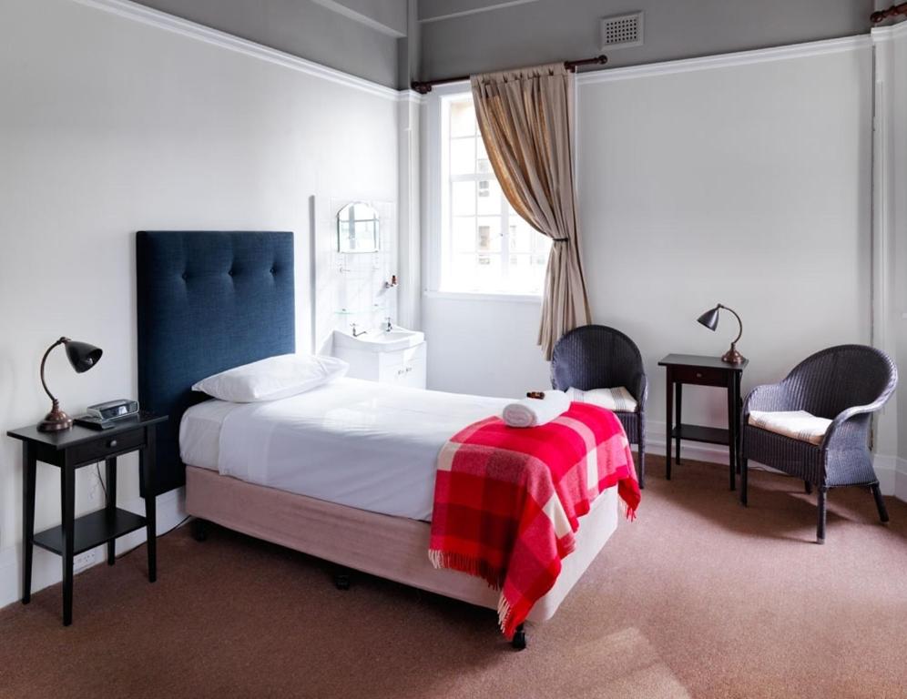 a bedroom with a bed with a red blanket and two chairs at Grand Hotel Sydney in Sydney