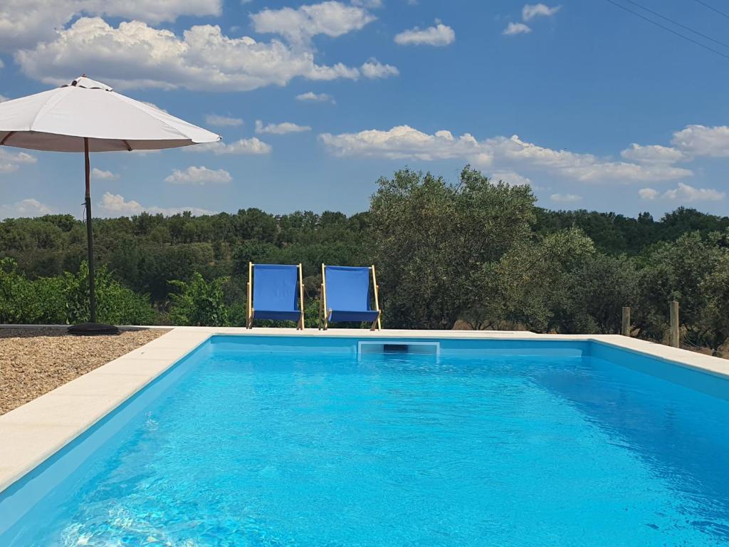 a swimming pool with two chairs and an umbrella at Monte das Aranhas in Estremoz