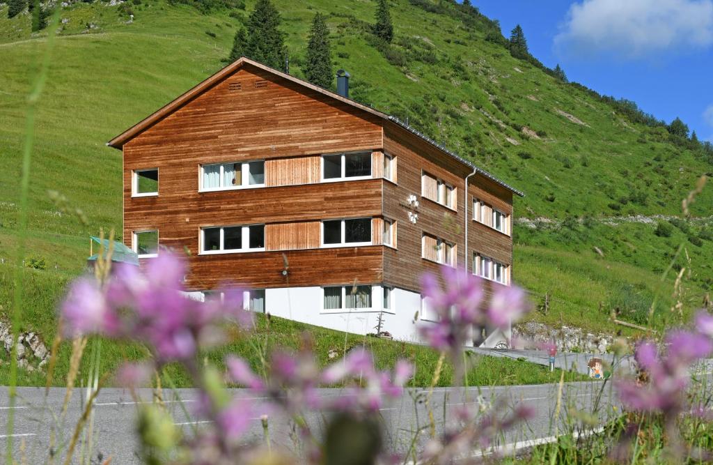 un bâtiment en bois au sommet d'une colline avec des fleurs violettes dans l'établissement Bergzeit Appartements, à Warth am Arlberg