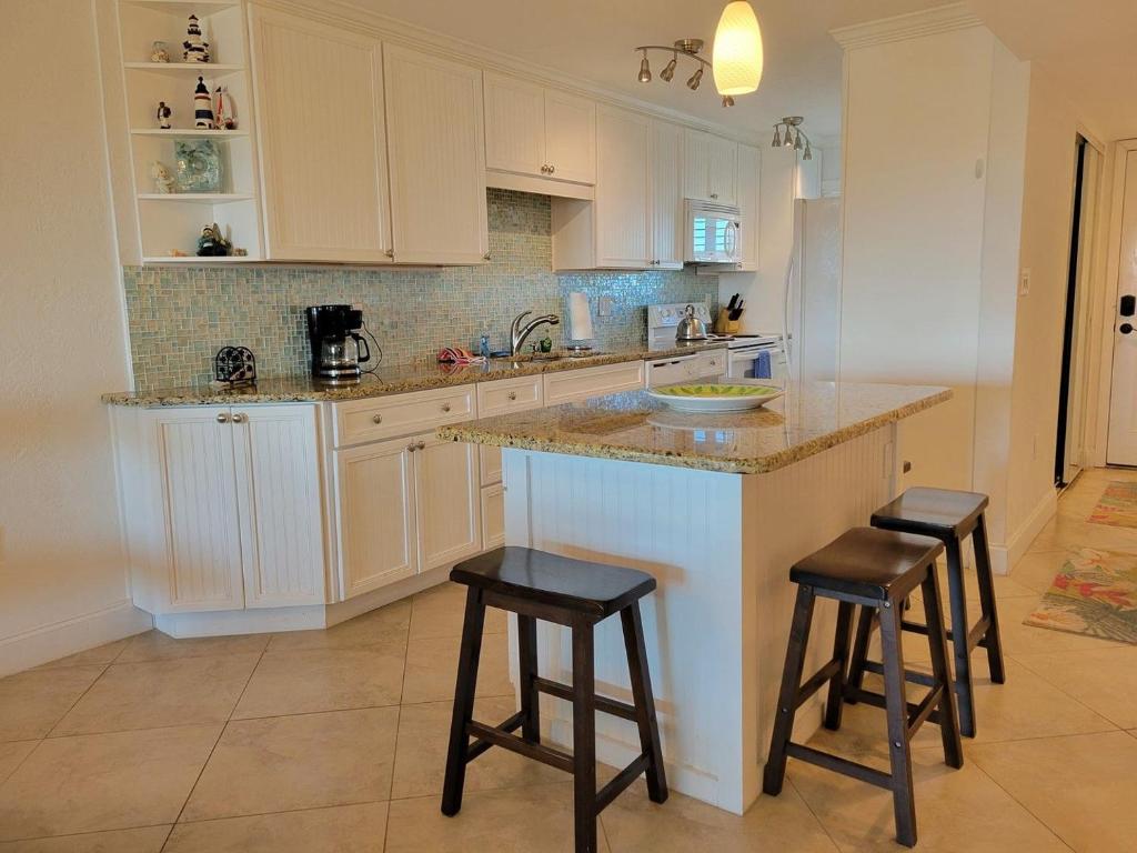 a kitchen with white cabinets and a island with stools at Hacienda del Sol II - 404 in New Smyrna Beach