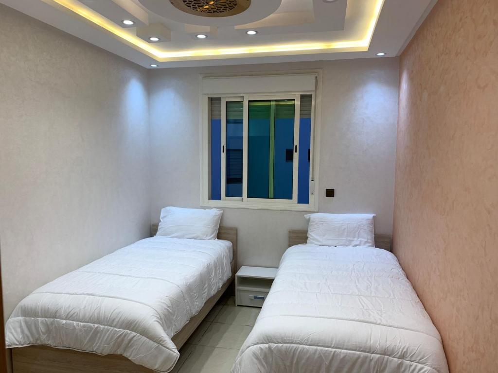 - 2 lits dans une petite chambre avec fenêtre dans l'établissement Résidence Le joyau de la mer Plage Des Nations, à Sidi Bouqnadel