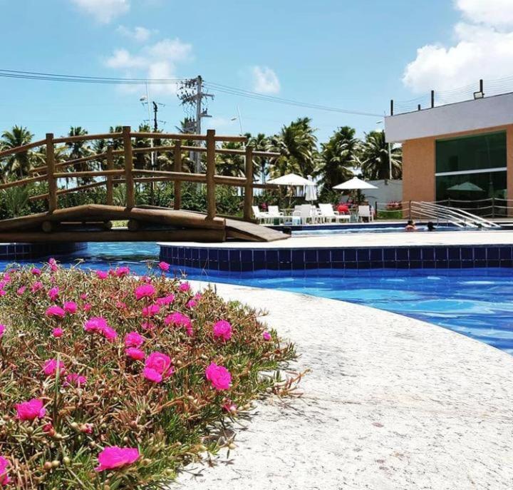 a swimming pool with pink flowers and a bridge at MURO ALTO COND CLUBE Bl4 413 in Ipojuca
