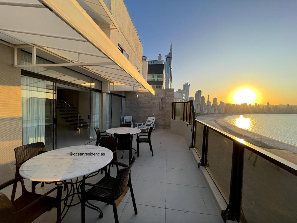 a balcony with tables and chairs and a view of the water at Cobertura Quebec Beira-Mar in Balneário Camboriú
