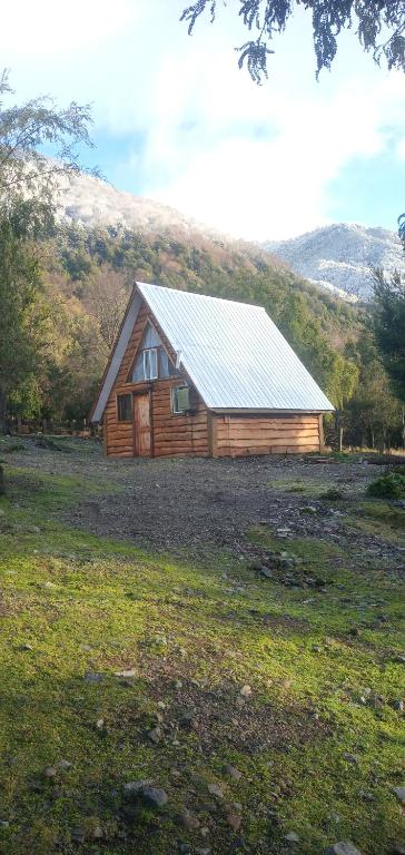 uma cabana de madeira num campo com uma montanha em Cabaña Nawel em Melipeuco
