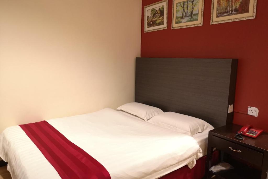 a bedroom with a white bed and a red wall at OYO 89908 Hotel Kensington in Sandakan