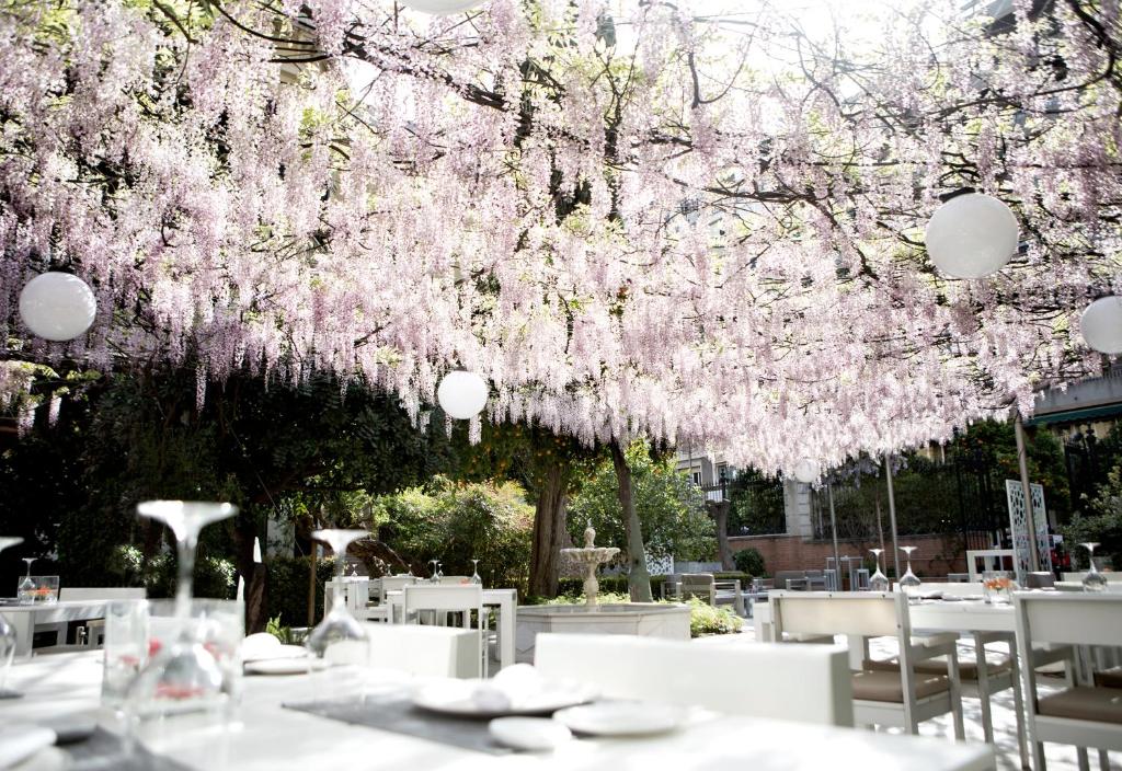 a restaurant with tables and chairs under a tree with pink flowers at Hospes Palacio de los Patos in Granada